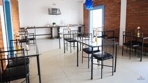 A dining area with black metal chairs and tables, a brick wall, a television, and a blue door. - Rafas Pousada Encantos de Minas  (Tres Coracoes)