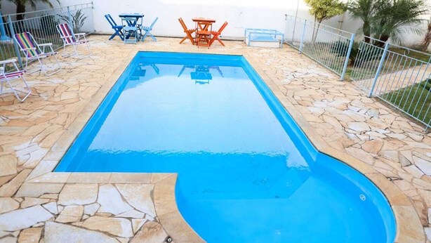 A rectangular swimming pool with a stone border, surrounded by lounge chairs and tables. - Rafas Pousada Encantos de Minas  (Tres Coracoes)