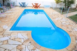 Ein rechteckiger Swimmingpool mit Steinrand, umgeben von Liegestühlen und Tischen.