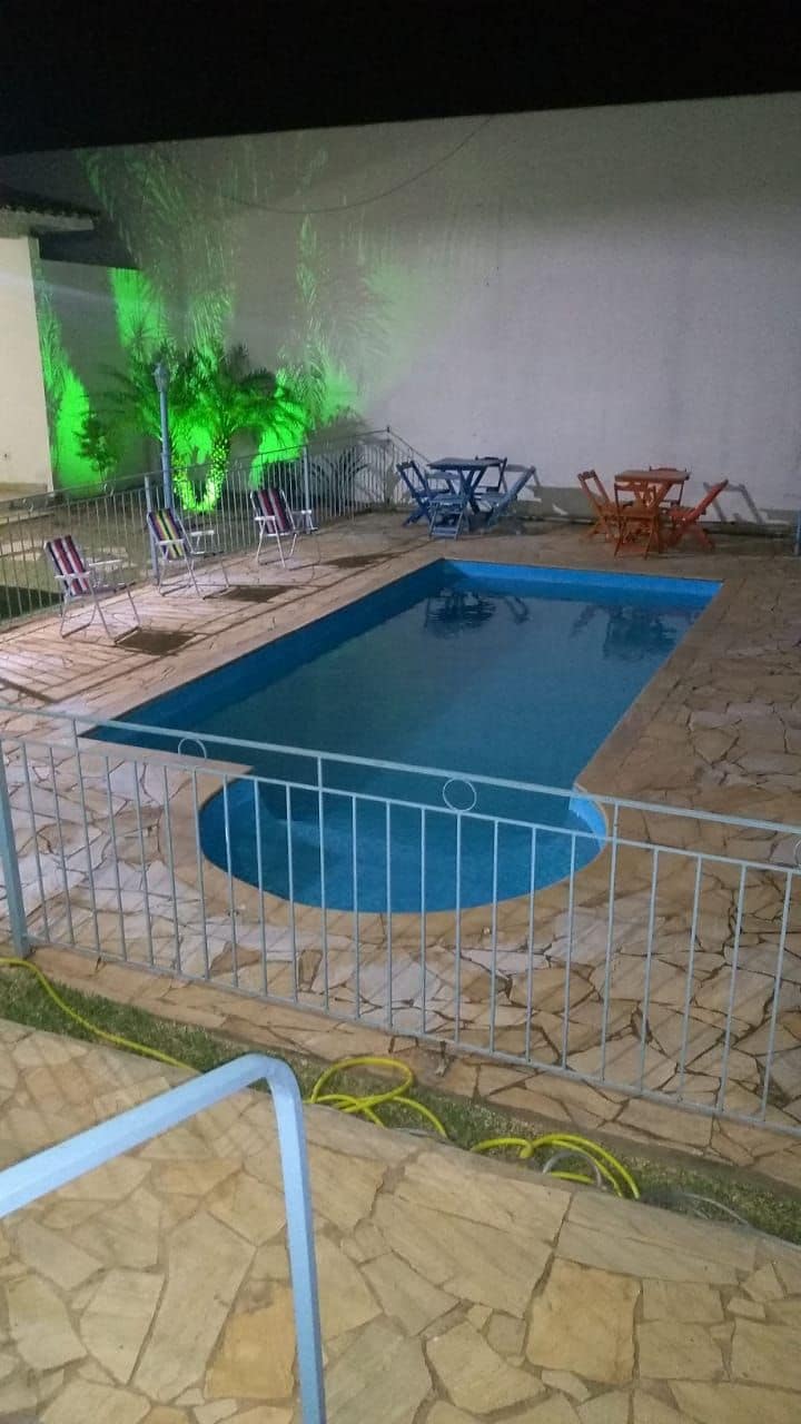 Piscina ao ar livre com deck de pedra, cercada por uma grade de metal, e equipada com espreguiçadeiras e mesas.
