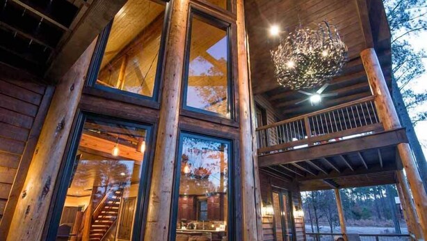 A log cabin with a large window, a staircase, and a balcony.