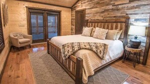 A bedroom with a wooden headboard, a bed with patterned bedding, a chair, and a small table with a lamp.