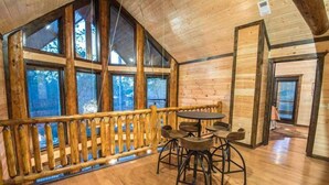 A wooden interior with large windows, a wooden deck, and a round table with chairs.