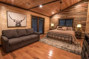 A log cabin bedroom with a bed, a sofa, and a framed animal picture.