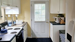 A compact kitchen with white cabinets, a stove, a microwave, and a sign that reads "OUR HAPPY PLACE".