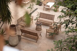 Een terras met rieten meubilair, waaronder een bank, stoelen en een tafel, omgeven door potplanten en grote vazen.