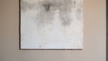 Une pièce dans laquelle on trouve un grand tableau abstrait au mur, un banc en bois et un vase vert.