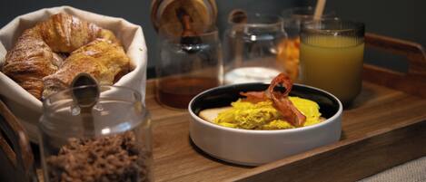 A breakfast tray with croissants, scrambled eggs with bacon, a bowl of chocolate spread, and a glass of orange juice.