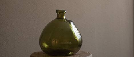 A green vase on a wooden stool against a plain wall.