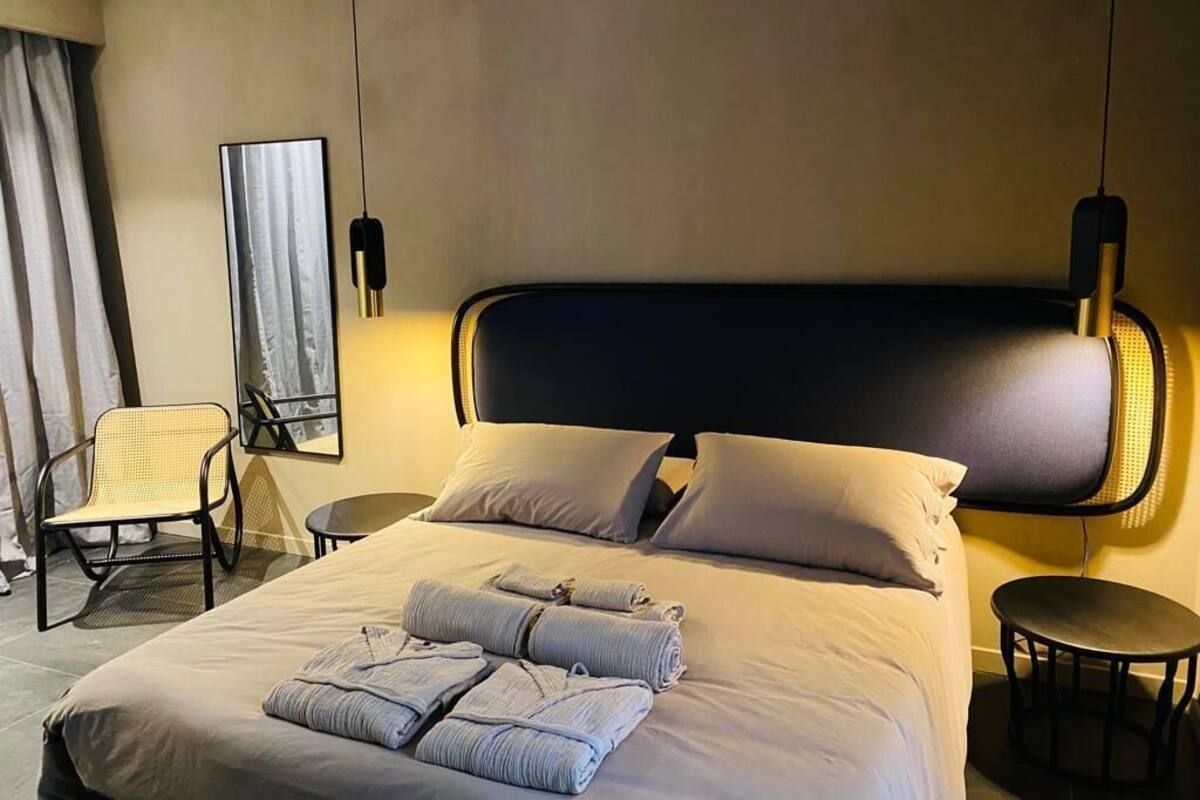 A hotel room with a large bed, two bedside tables, a chair, a mirror, and a hanging light fixture.