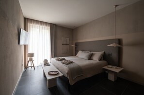 Een moderne hotelkamer met een groot bed, nachtkastjes, een flatscreen televisie en een raam met gordijnen.