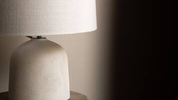A table lamp with a white shade on a wooden stool against a plain wall.