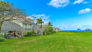 A residential property with a well-maintained lawn, a patio with outdoor furniture, and a view of the ocean. - Split Level Home Perfect for Large Families & Groups Traveling Together! (Princeville)
