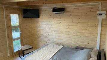 Et værelse i en træhytte med en seng, et lille bord, et fjernsyn monteret på væggen og et vindue.