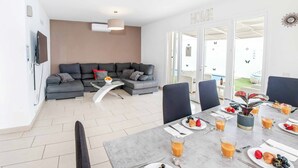 Un salon moderne avec un canapé gris, une table à manger dressée pour le petit-déjeuner et une vue sur l’extérieur.