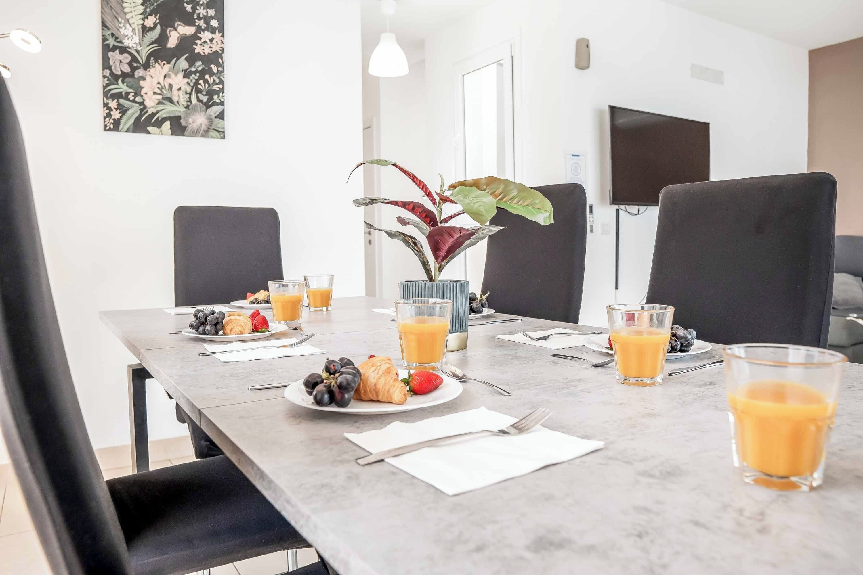 A dining table set with plates of food, glasses of orange juice, and a vase with a plant.