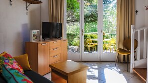 A living room with a sofa, a wooden cabinet, a TV, and a sliding glass door leading to an outdoor area with a table and chairs. - Le Triangle D'or - Le Chêne - Piscine - Gaillac (Gaillac)