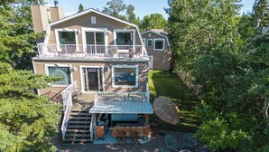A two-story house with a balcony, a patio with chairs and a table, and a fenced yard.