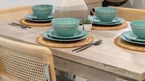 A dining area with a wooden table set with teal bowls and plates, a woven placemat, and a decorative vase with a palm frond.