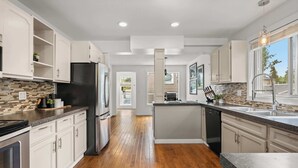 A modern kitchen with white cabinetry, a black refrigerator, and a wooden floor.
