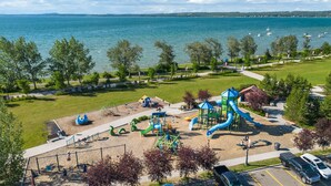 A park with playground equipment, a parking lot, and a view of a lake.