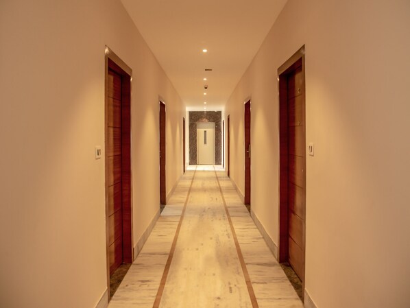 A long, narrow hallway with wooden doors on both sides, leading to a room at the end.