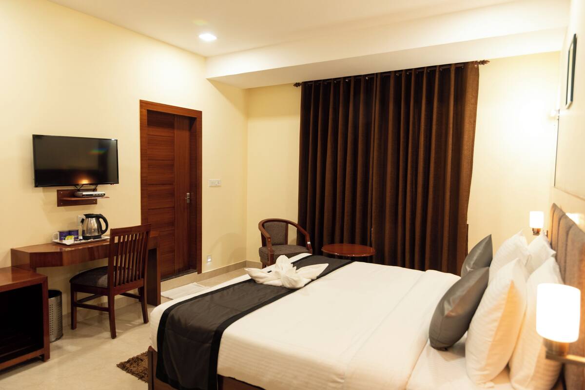 Una habitación de hotel con cama, escritorio con televisor, silla y ventana con cortinas.