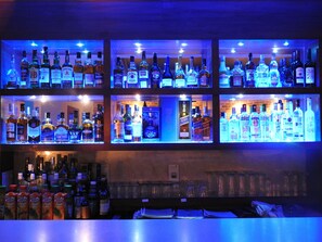 A bar with multiple shelves of liquor bottles, glasses, and a counter with various bottles and cans.