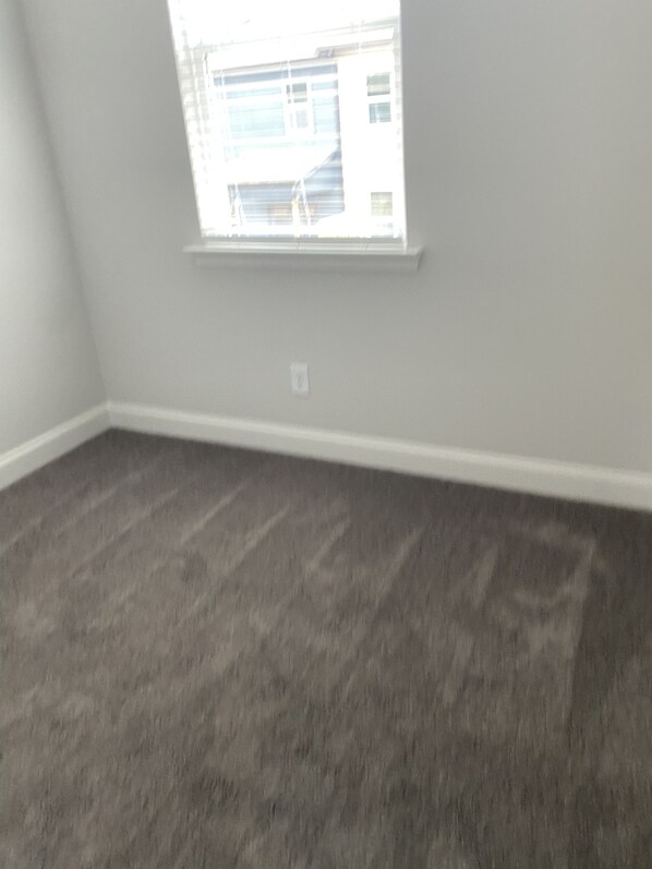 A room with a large window, carpeted floor, and white walls.