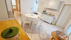 Ein Essbereich mit einem runden Tisch und vier Stühlen, eine Küche mit weißen Schränken und einem Spülbecken sowie ein kleines dekoratives Teller auf einem Beistelltisch.