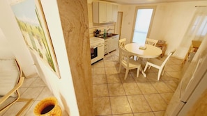 A kitchen with white cabinets, a dining table with four chairs, and a tiled floor.