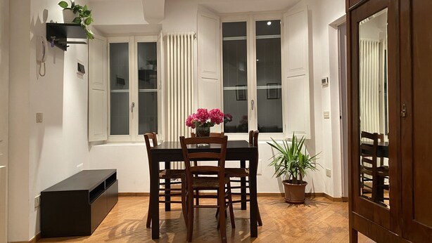 A dining area with a table and chairs, a potted plant, and a radiator. - Apartment that sleeps 4 a stone's throw from Parma Cathedral (Parma)