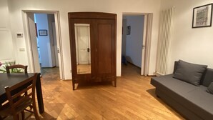 A living room with a wooden floor, a grey sofa, a dining table with chairs, and a door leading to another room. - Apartment that sleeps 4 a stone's throw from Parma Cathedral (Parma)