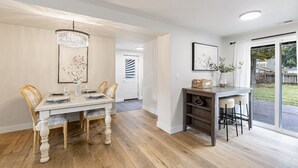 Un espace repas comprenant une table et des chaises en bois, un lustre et un petit coin bar avec des tabourets.
