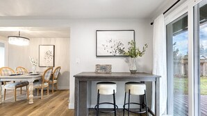 Une cuisine moderne avec un coin repas, comprenant une table en bois, des tabourets de bar et une grande fenêtre donnant sur l’extérieur.