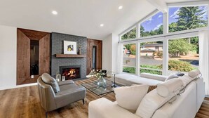 Een moderne woonkamer met een open haard, een bank en een groot raam met uitzicht op de omgeving.