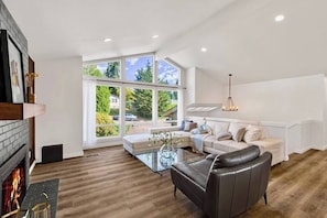 A modern living room with a fireplace, large windows, a glass coffee table, and a leather sofa.