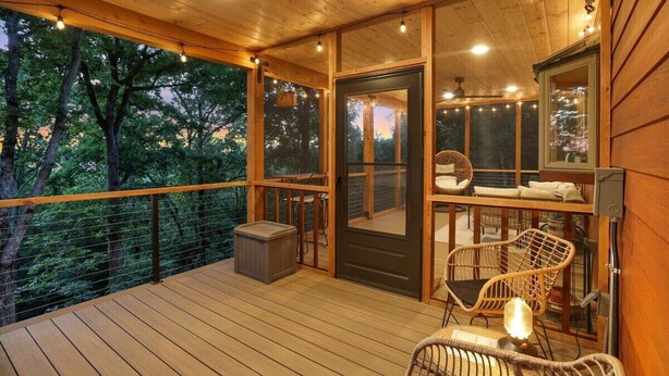 Une terrasse en bois avec une porte vitrée donnant sur une pièce, le tout entouré d’arbres.
