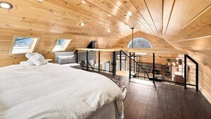 Une chambre dotée d’un grand lit, d’un bureau et offrant une vue sur l’extérieur grâce à une lucarne.