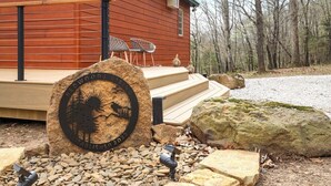 Une cabane en bois avec une plaque de pierre, des sièges à l’extérieur et un chemin de gravier.