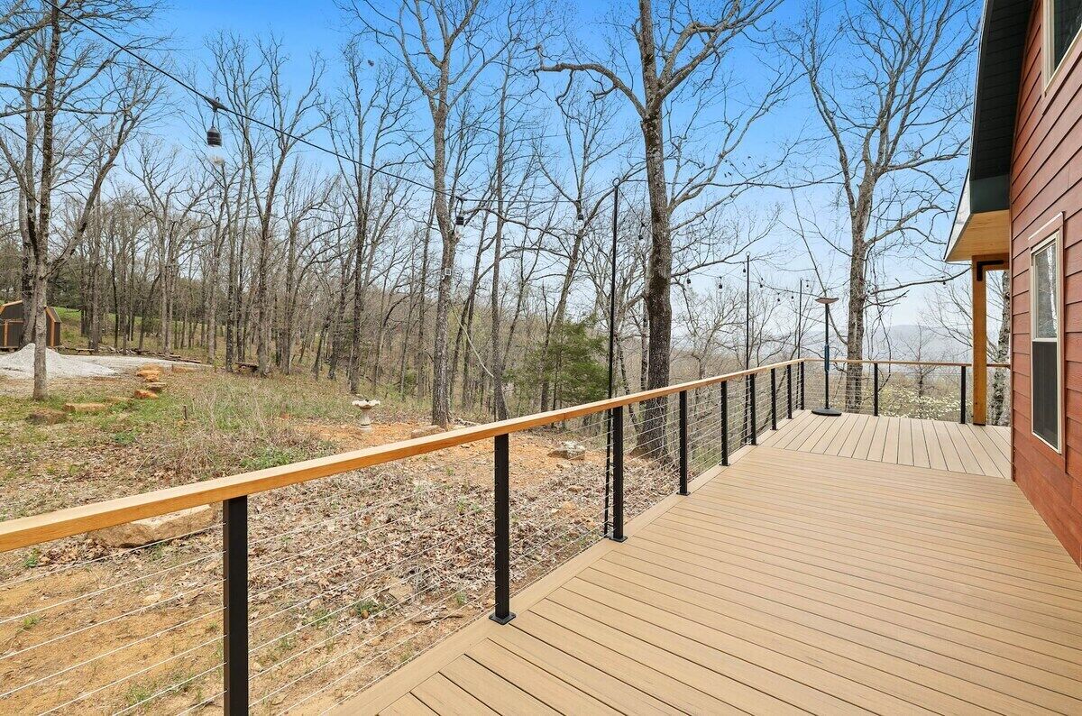Une terrasse en bois avec une rambarde en métal, entourée d’arbres et sous un ciel dégagé.