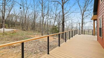 Une terrasse en bois avec une rambarde en métal, entourée d’arbres et sous un ciel dégagé.