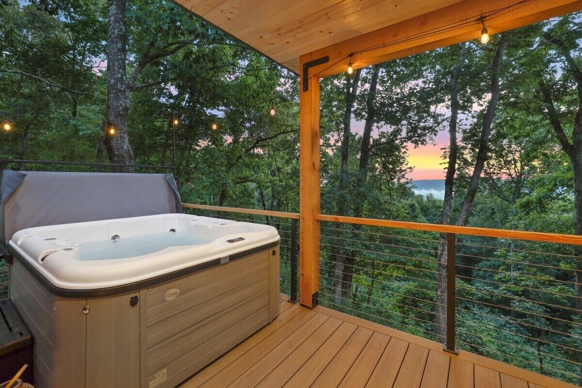 A hot tub on a wooden deck with a view of trees and a sunset.