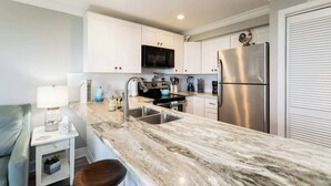 A modern kitchen with white cabinets, stainless steel appliances, a marble countertop, and a built-in microwave. - Sea View and Sunrise Ocean Pointe 2412 2BA/2BR (Tavernier)