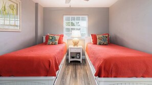 A bedroom with two single beds, each with a red bedspread and matching pillows, a bedside table with a lamp, and a framed picture on the wall.