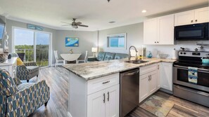 A modern kitchen with white cabinetry, a granite countertop, stainless steel appliances, and a view of the outdoors.