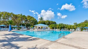 A pool area with lounge chairs and umbrellas, surrounded by palm trees and a covered pavilion. - Sea View and Sunrise Ocean Pointe 2412 2BA/2BR (Tavernier)
