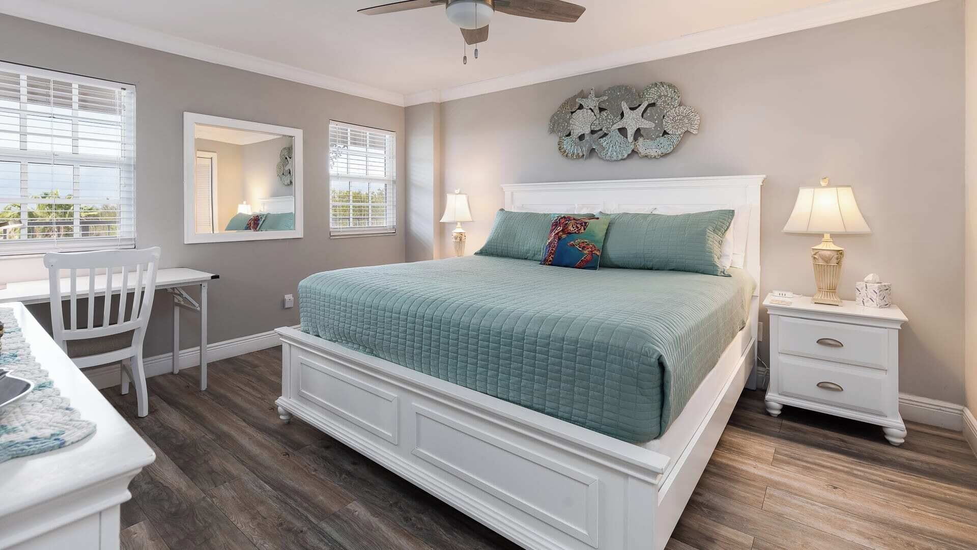 A bedroom with a bed, a desk, a chair, a nightstand, and a ceiling fan.
