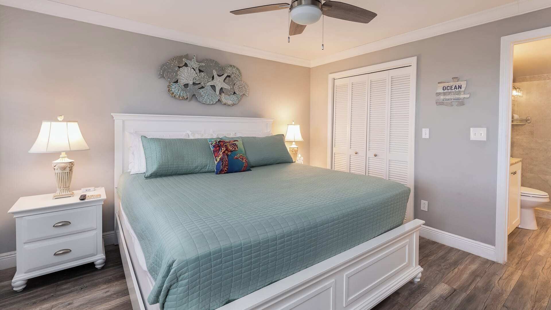 A bedroom with a bed, nightstands, a ceiling fan, a decorative wall piece, and a closet.