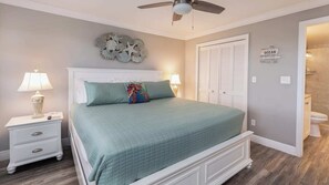 Un dormitorio con cama, mesitas de noche, ventilador de techo, un adorno en la pared y un armario.